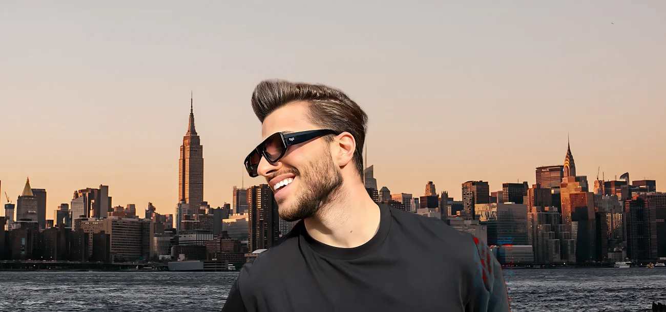 Smiling man wearing black square OJO sunglasses with New York City skyline at sunset – urban eyewear lifestyle shot